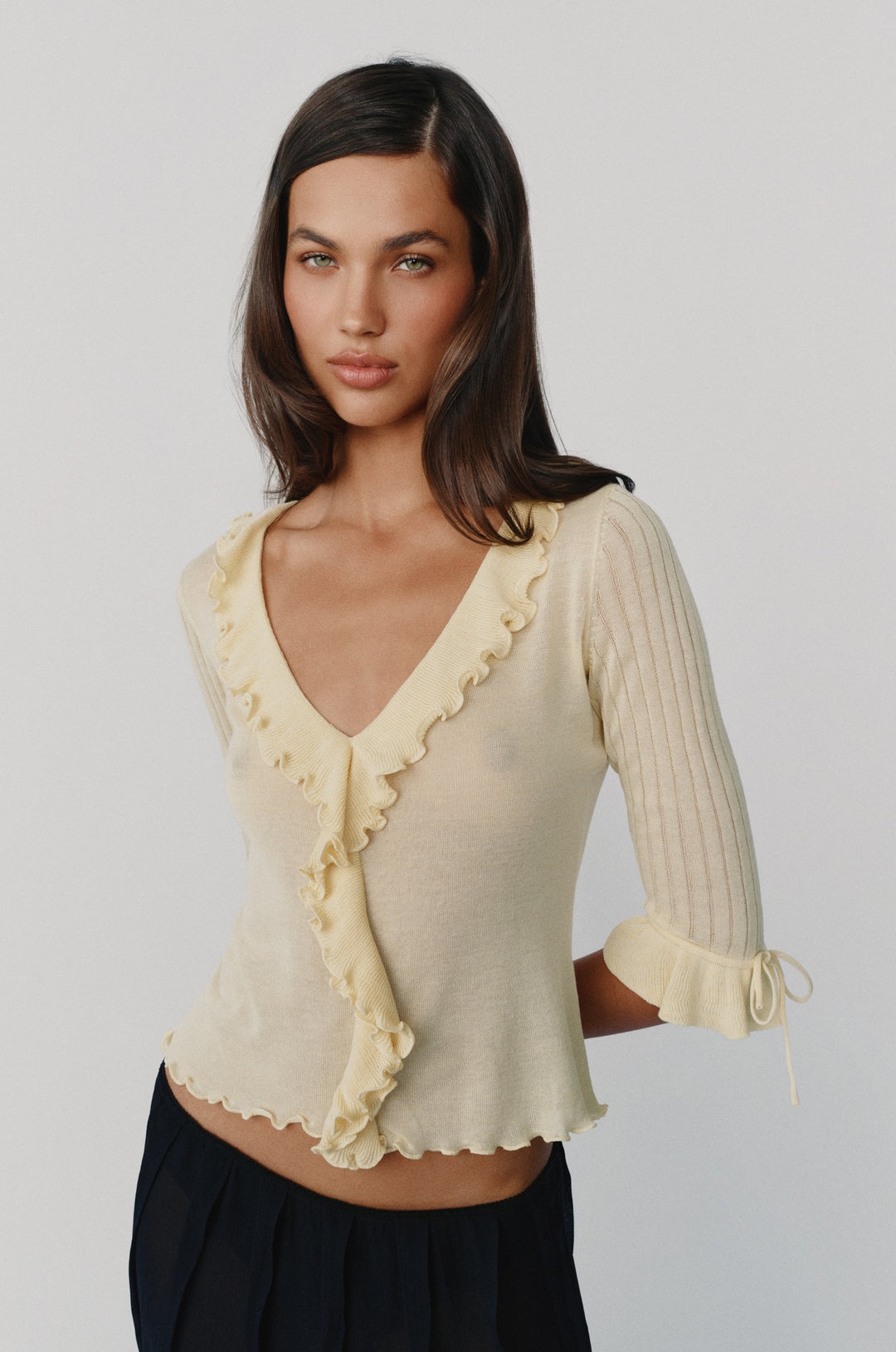 Pale yellow semi-sheer knitted top with ruffle-trim neckline, 3/4 sleeves, and tie-detail ruffle cuffs.