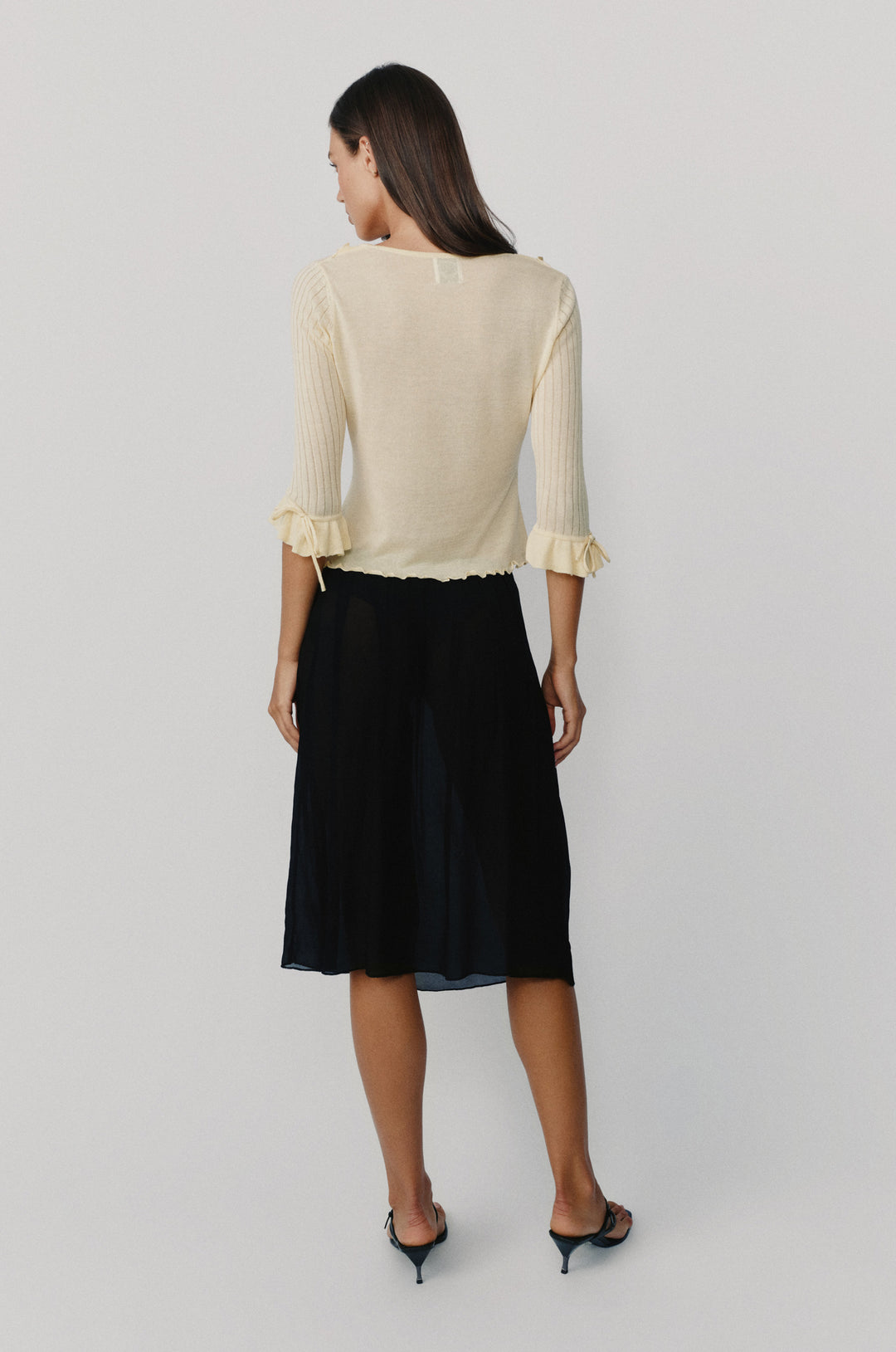 Pale yellow semi-sheer knitted top with 3/4 sleeves, ruffle cuffs with tie details, and a ruffle-trim neckline.