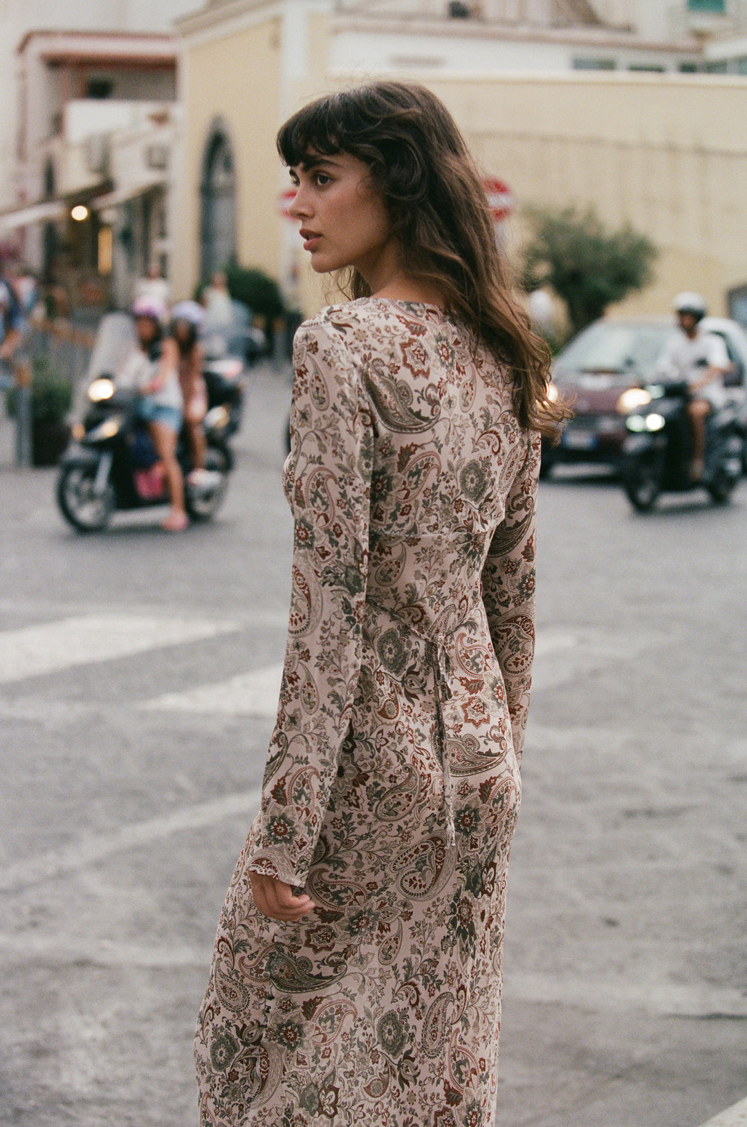 Josephine dress in stone paisley print featuring long sleeves, a sheer finish, and a back tie detail on a city street.