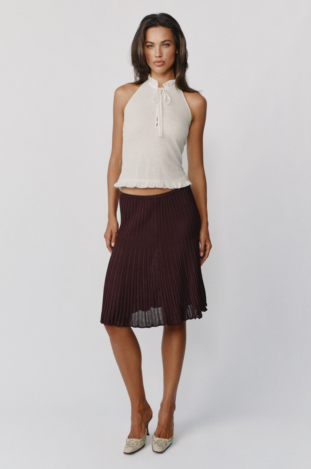 White knitted halter top with a self-tie neckline, button-front closure, and ruffle trim at the neck and hem.