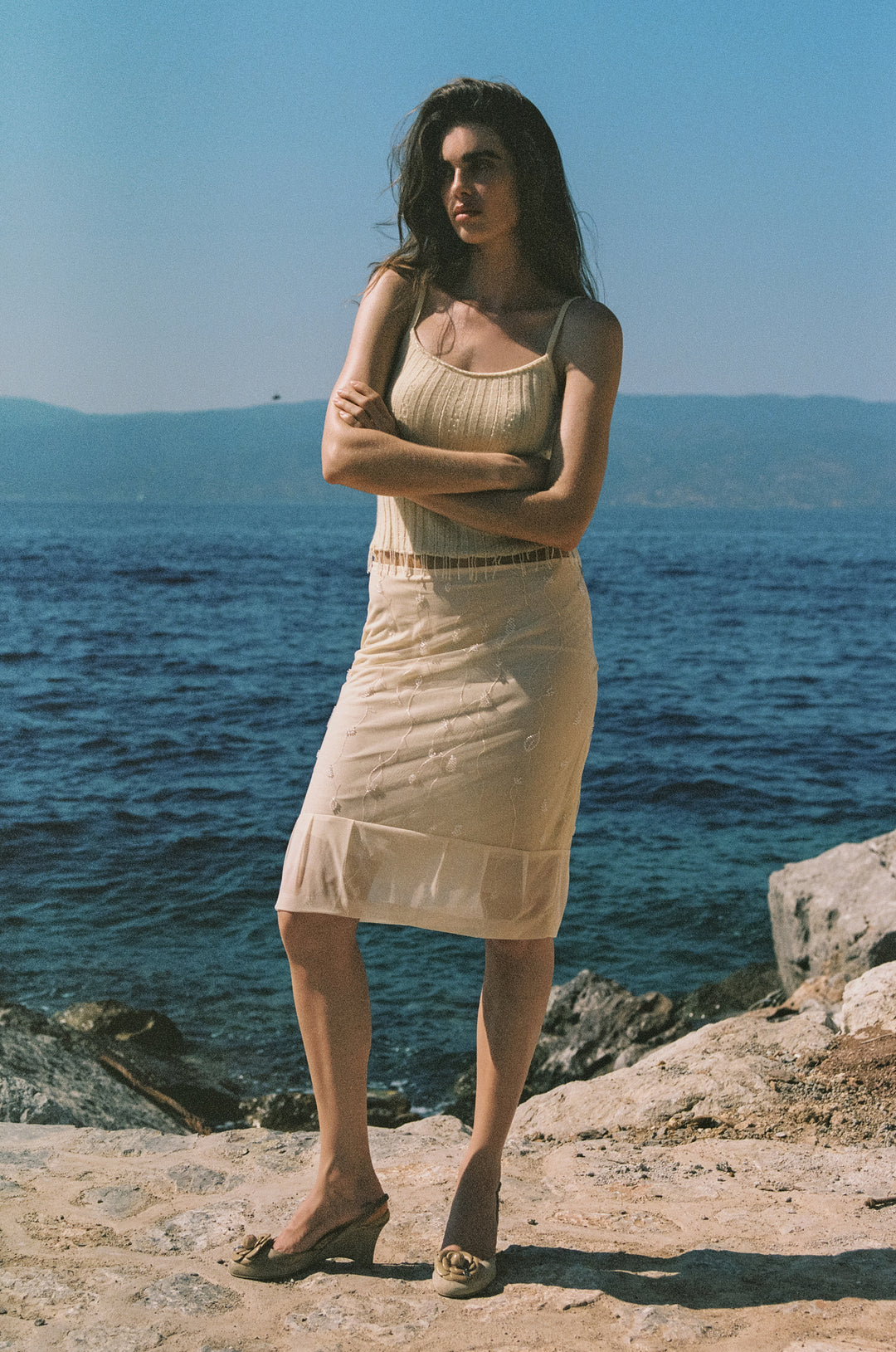Champagne semi-sheer midi skirt with vine embroidery, beaded detailing, and a pleated hem worn by the ocean.