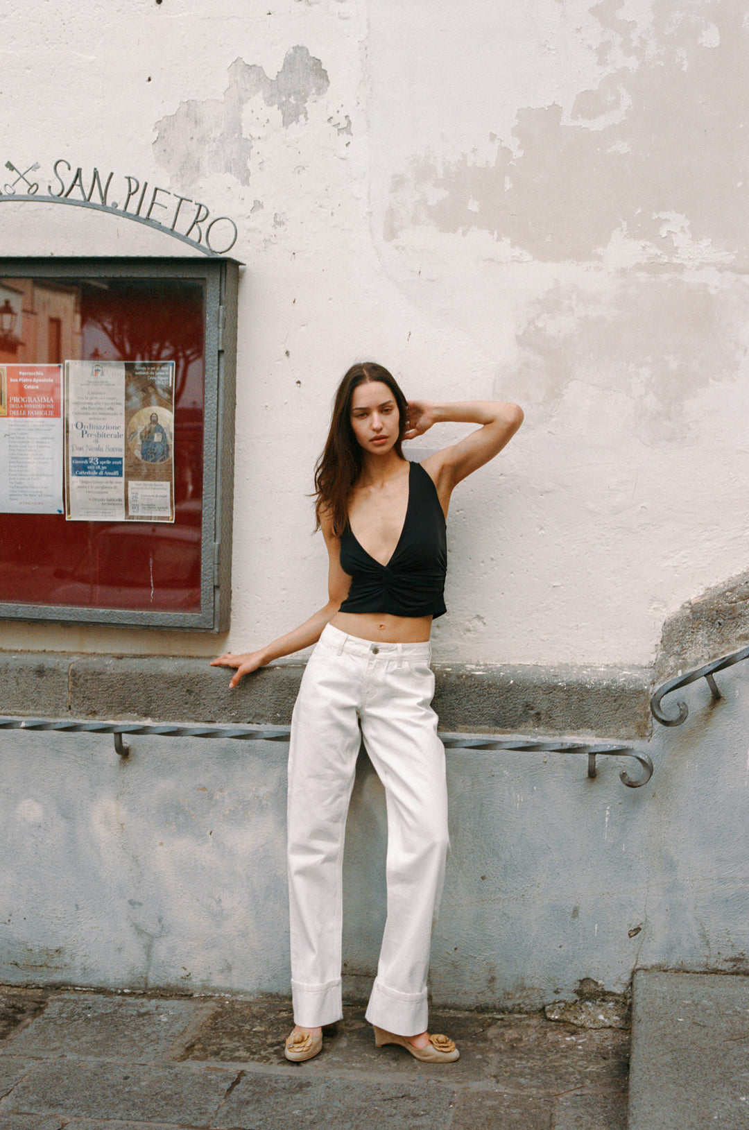 Woman in white Agnes low-rise selvedge denim jeans with fixed cuffed hem, black top, and beige sandals.