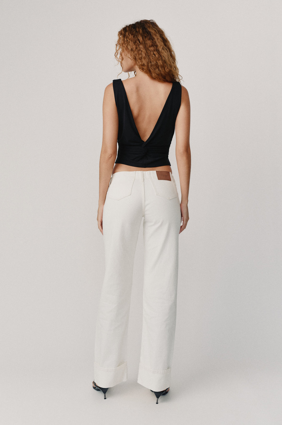 Woman from behind in white low-rise selvedge Agnes Jeans with fixed cuffed hem and a black top.
