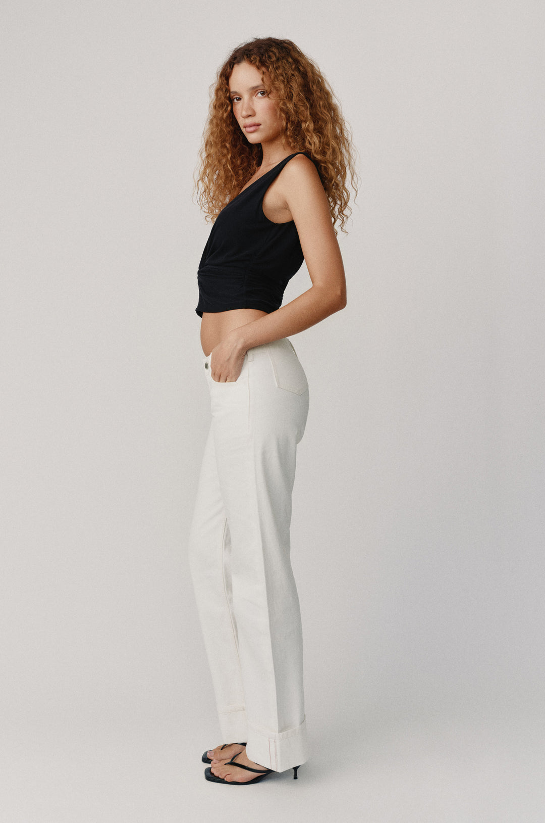 Woman in white Agnes low-rise selvedge denim jeans with fixed cuffed hem and black top.