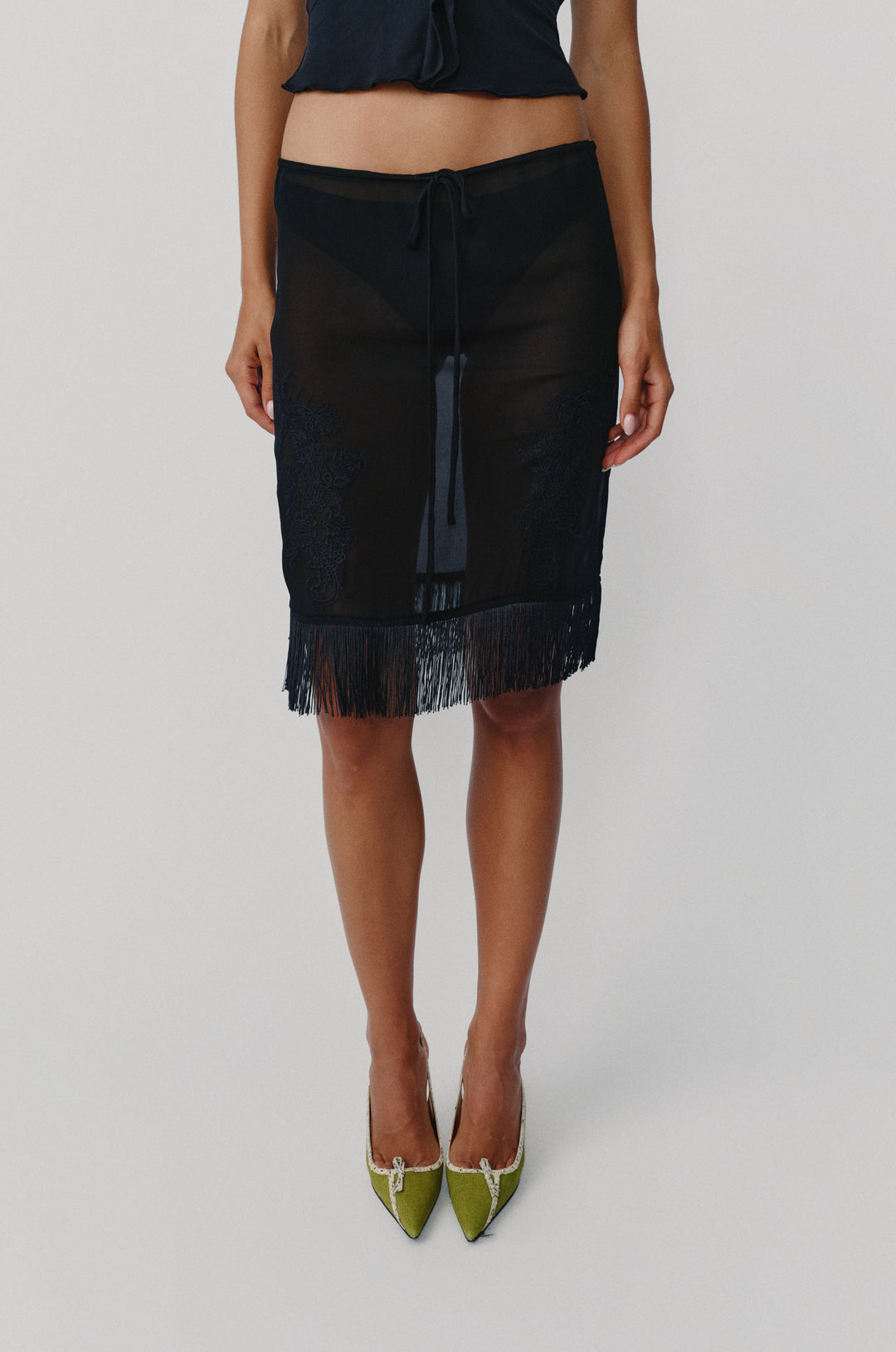 Sheer black low-rise Andie skirt with an adjustable drawstring waist, embroidered front detailing, and a fringe hem.