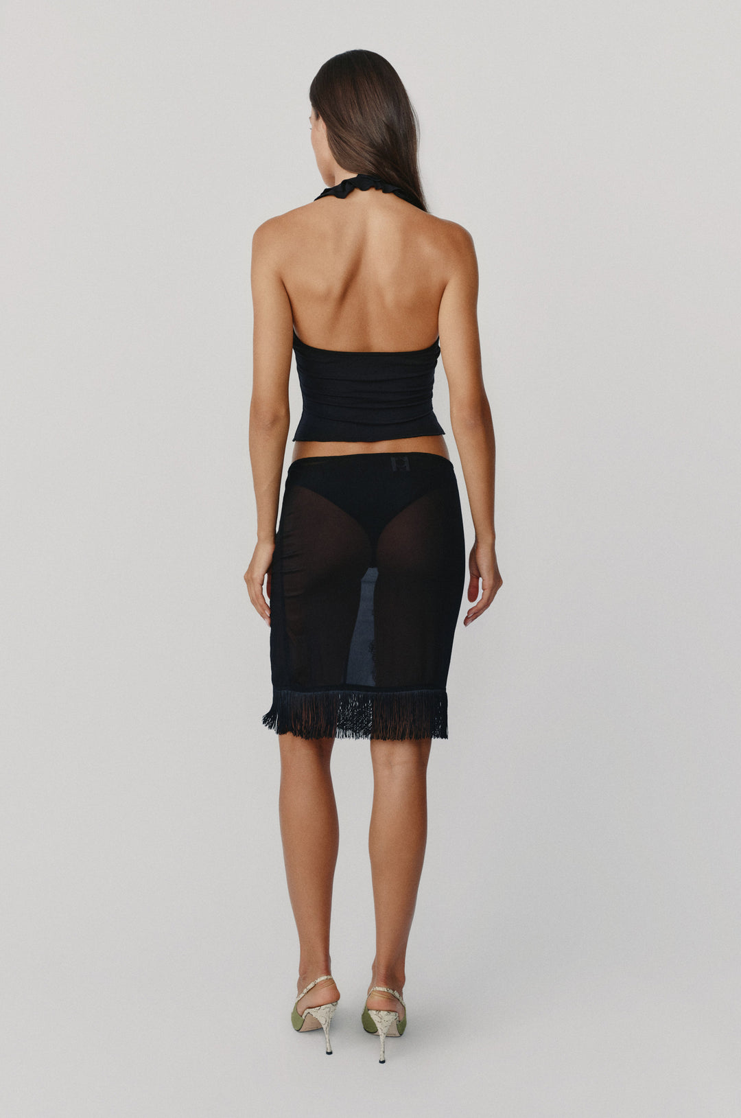 Black sheer low-rise Andie skirt with a fringe hemline, worn over a bikini bottom against a neutral background.
