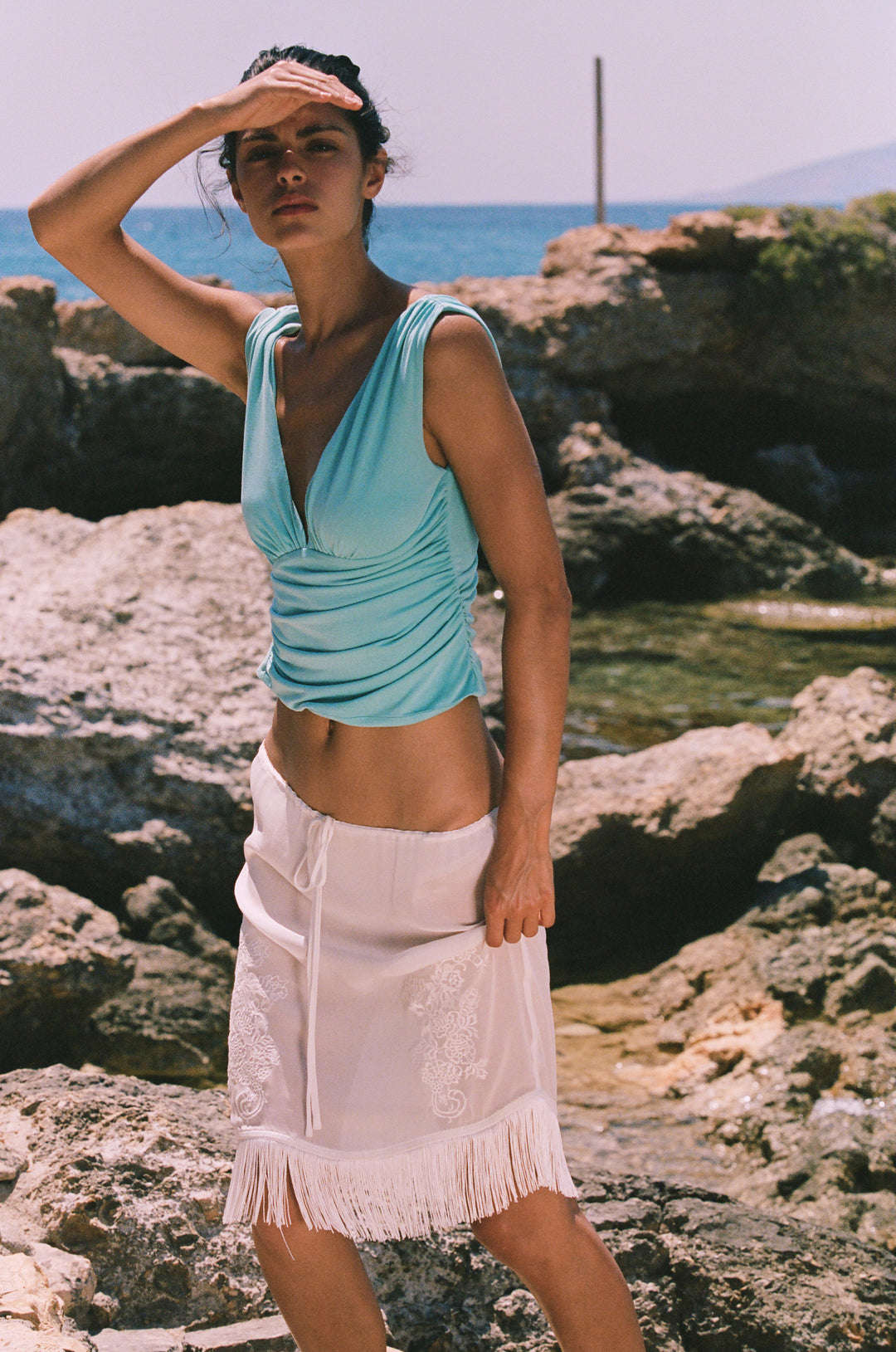 White low-rise Andie skirt featuring an adjustable drawstring waist, intricate floral embroidery, and a fringe hemline.