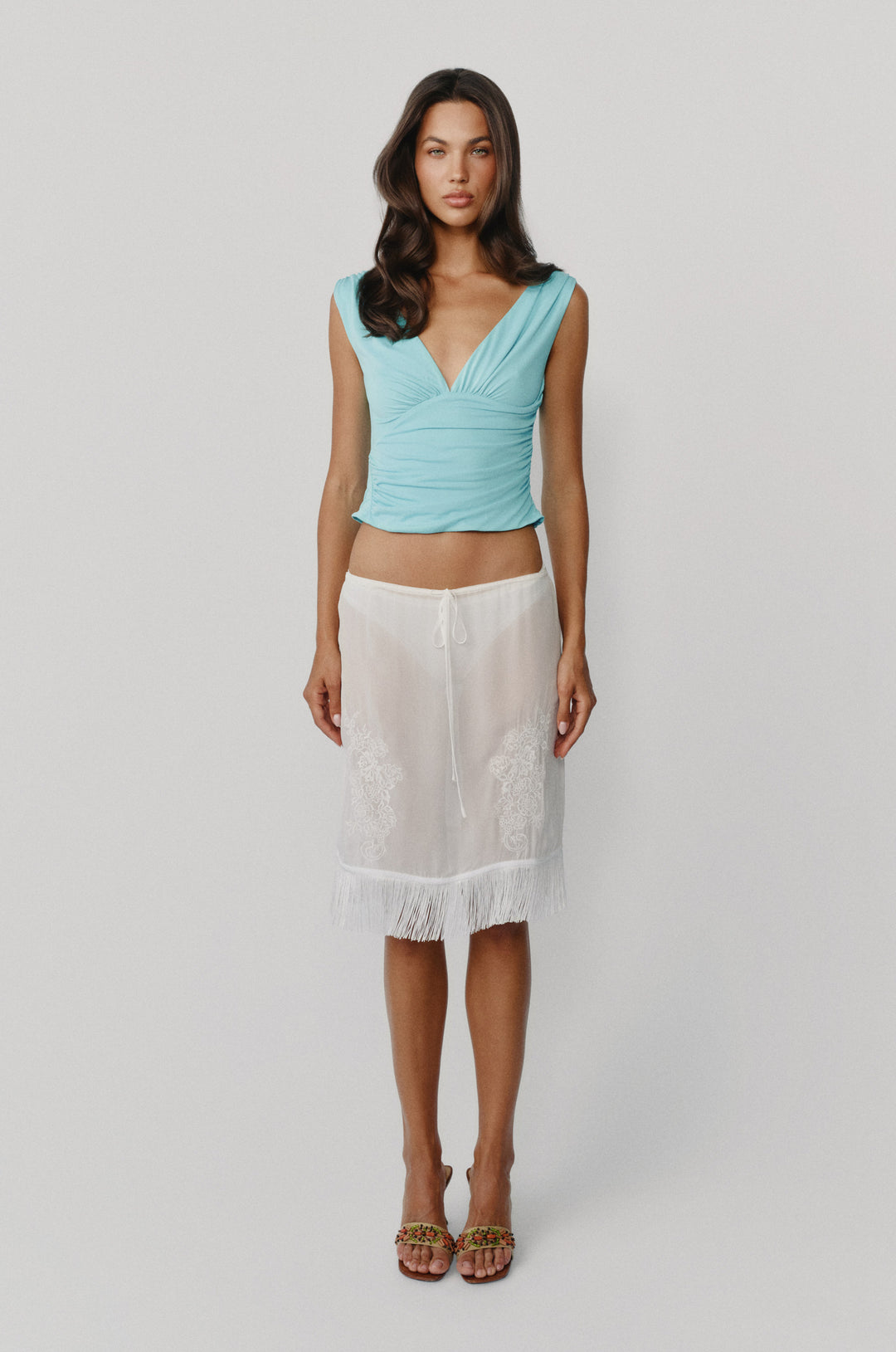 Low-rise white Andie skirt with an adjustable drawstring waist, delicate front embroidery, and a fringe hemline.