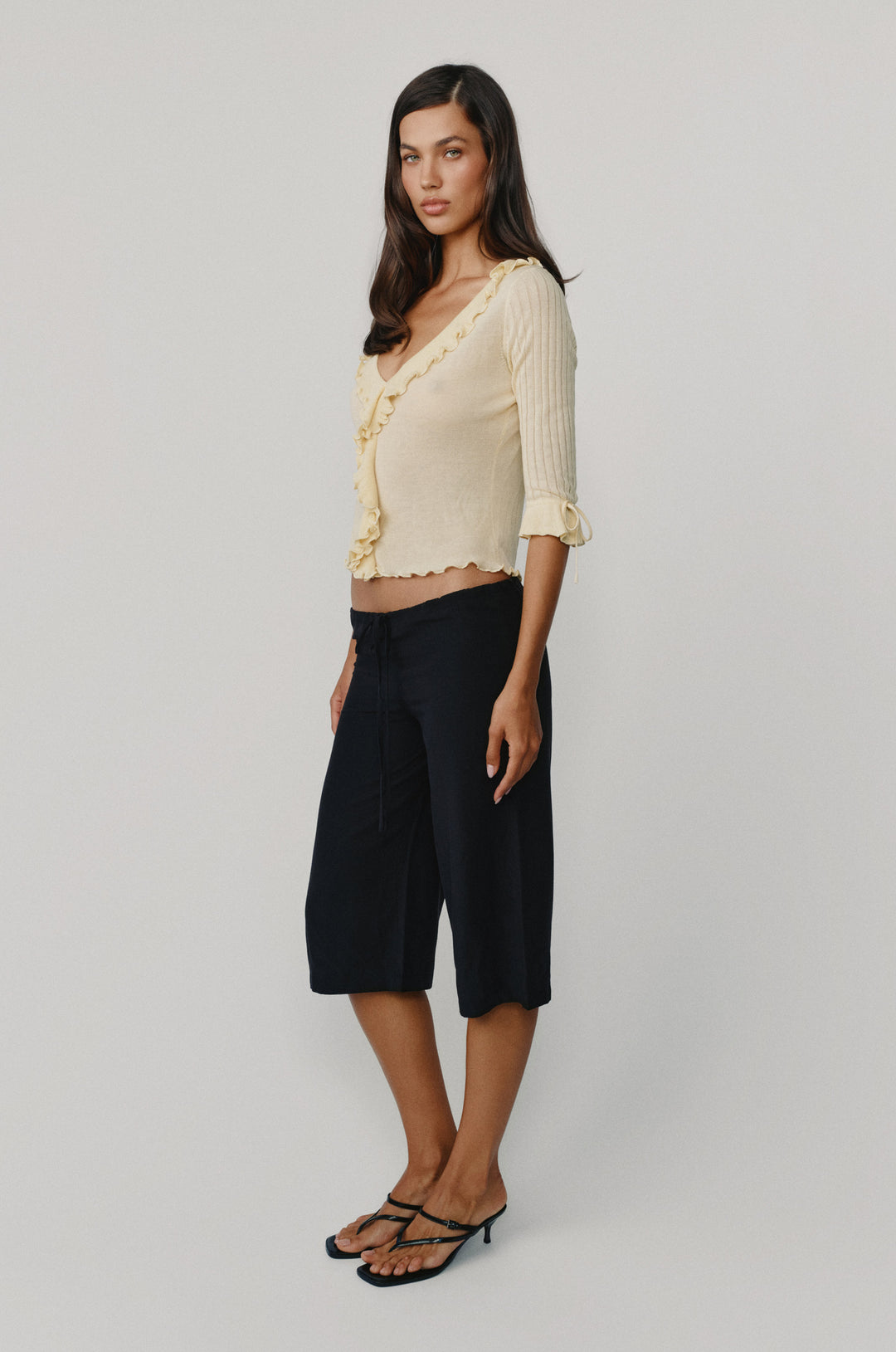 Model wearing black low-rise, relaxed-fit Arden Capri pants with an adjustable tie waistband paired with a cream ruffled top.