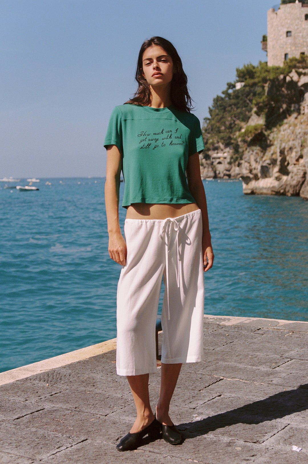 Woman wearing white Arden Capri Pant with adjustable tie waistband and a green t-shirt by the sea.