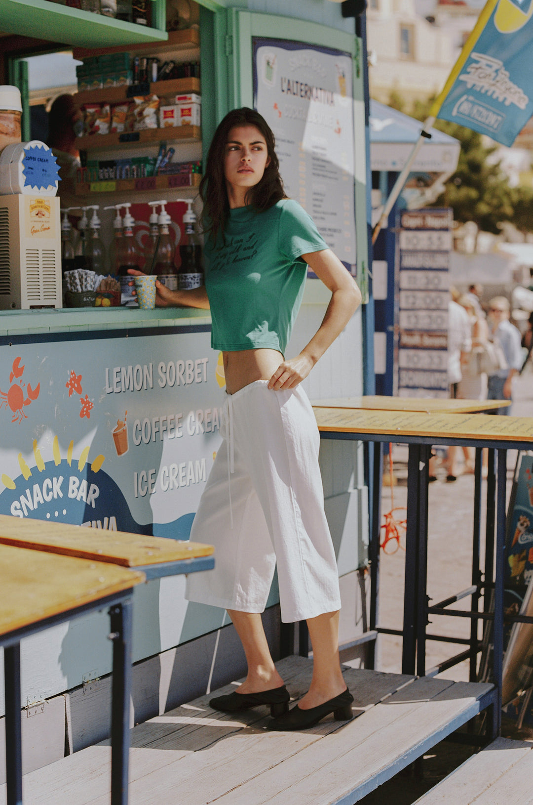 Woman in white Arden Capri Pant with adjustable tie waistband and green crop top at a snack bar.