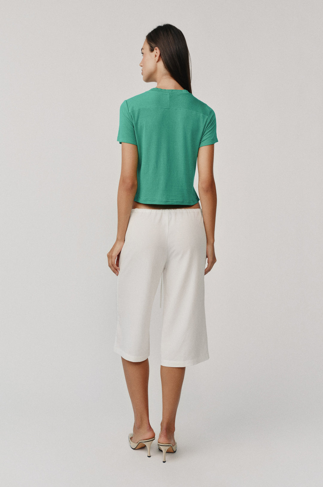 Woman from behind wearing white Arden Capri Pant with adjustable tie waistband and a green top.