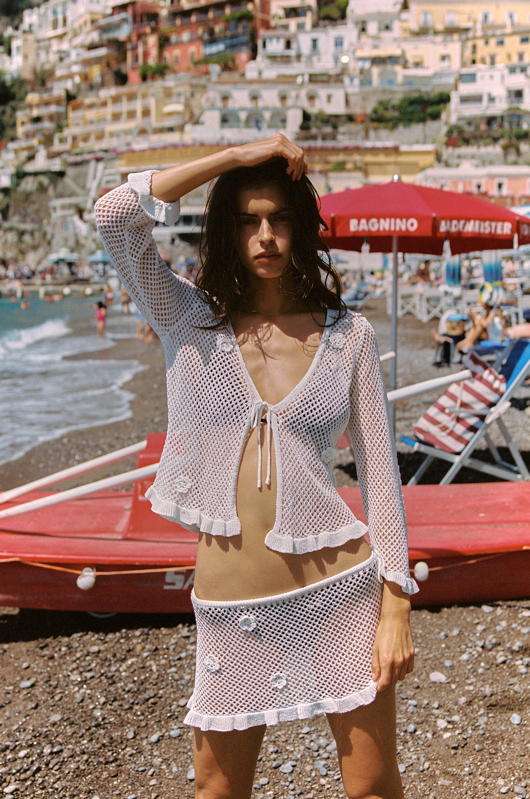 White knitted low-rise mini skirt with floral appliques and ruffle hem on a model at the beach.