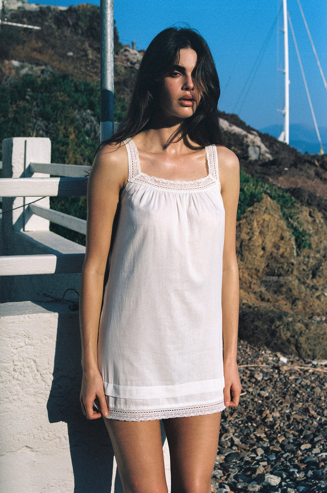 White lightweight cotton mini dress with delicate lace-trim straps, neckline, and hem worn outdoors.