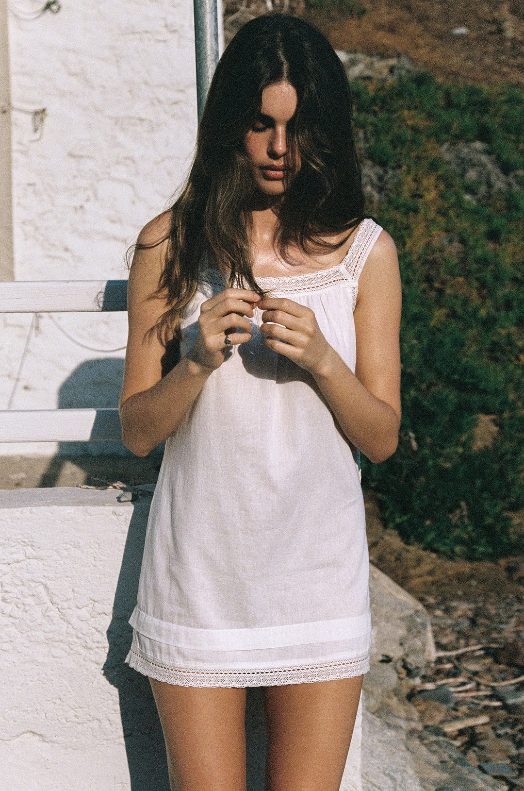 Arielle white cotton mini dress with delicate lace-trim straps, neckline, and hem, worn outdoors in sunlight.