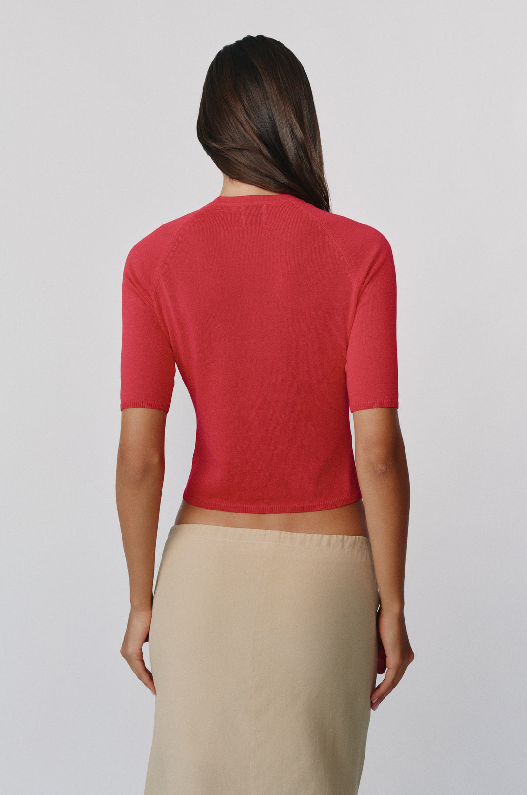 Back view of a red knit Avery top with half sleeves and a round neckline paired with a beige skirt.
