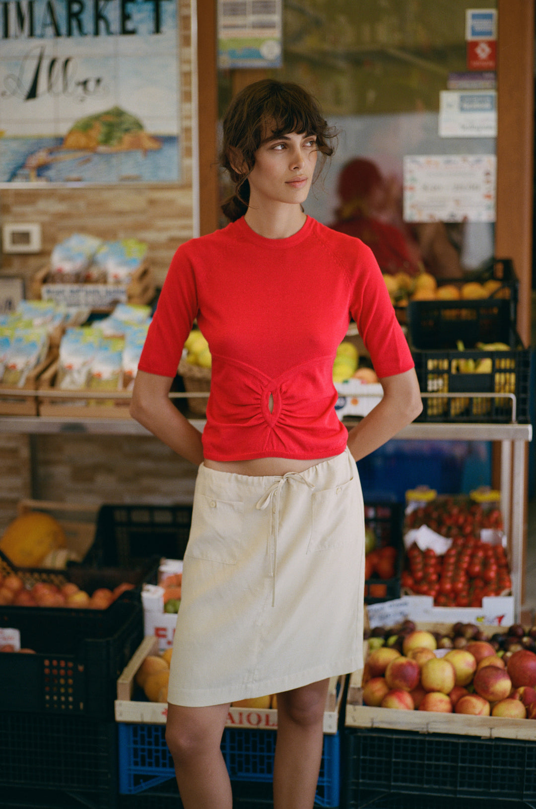 A woman wearing a red knit Avery top with half sleeves and a gathered keyhole cut-out, paired with a beige skirt.