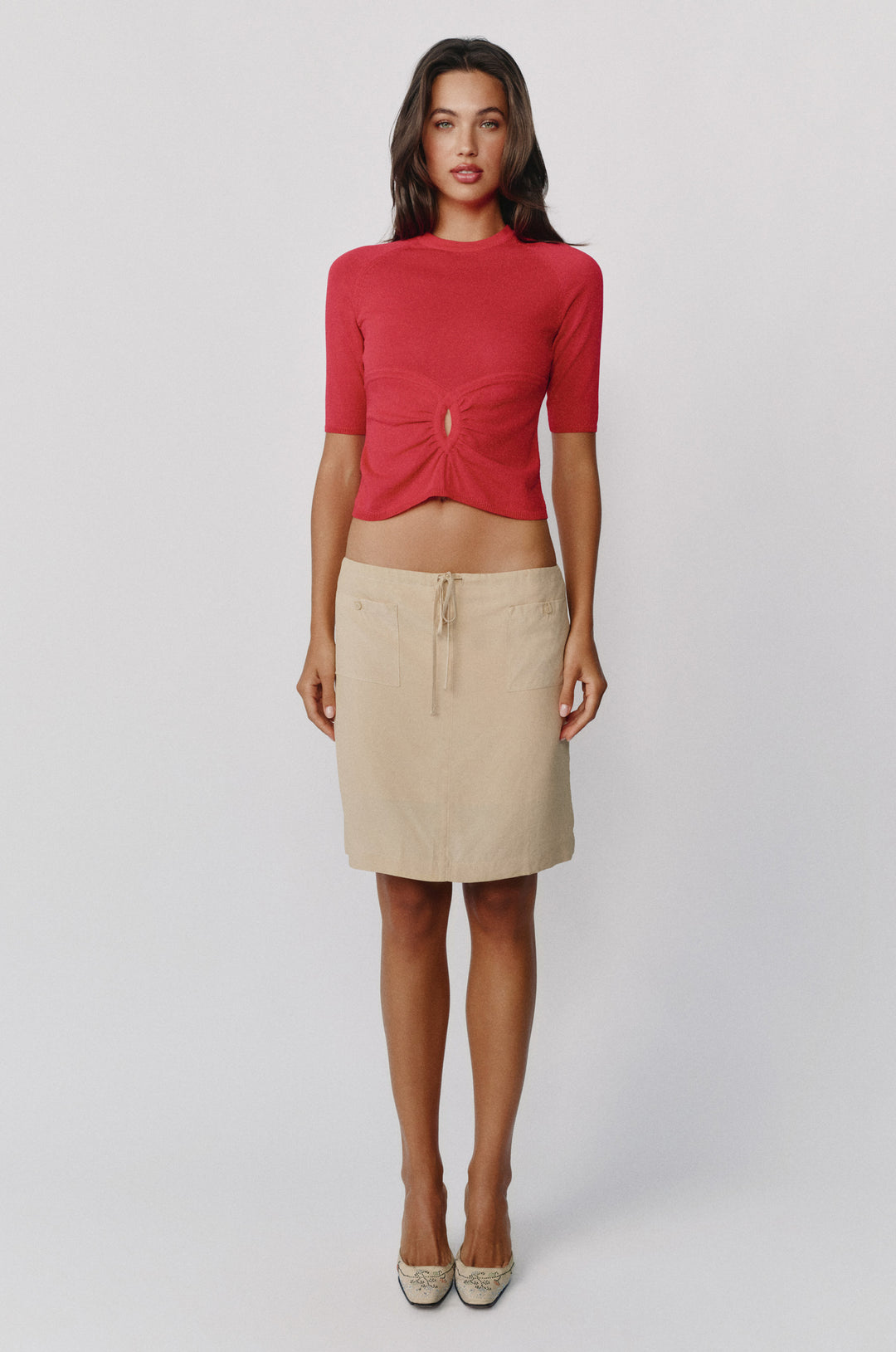 Red knit top with half sleeves, round neckline, and a gathered front keyhole cut-out paired with a beige skirt.
