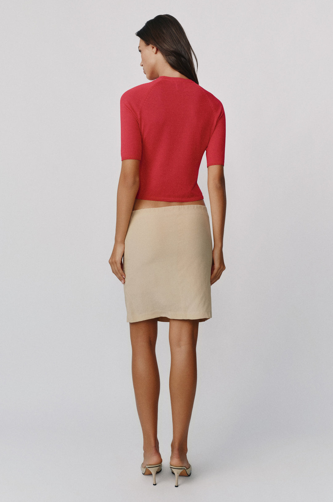 Back view of a red knit Avery top with half sleeves paired with a beige skirt on a model.