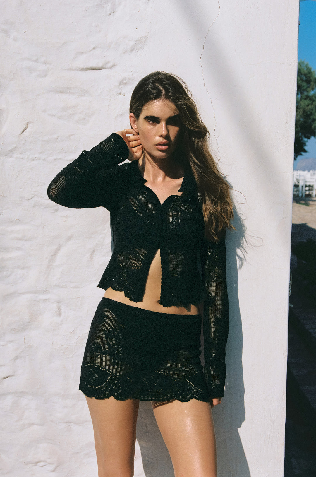 Black long-sleeve button-up cardigan in sheer crochet lace with a collared neckline and scalloped trim.