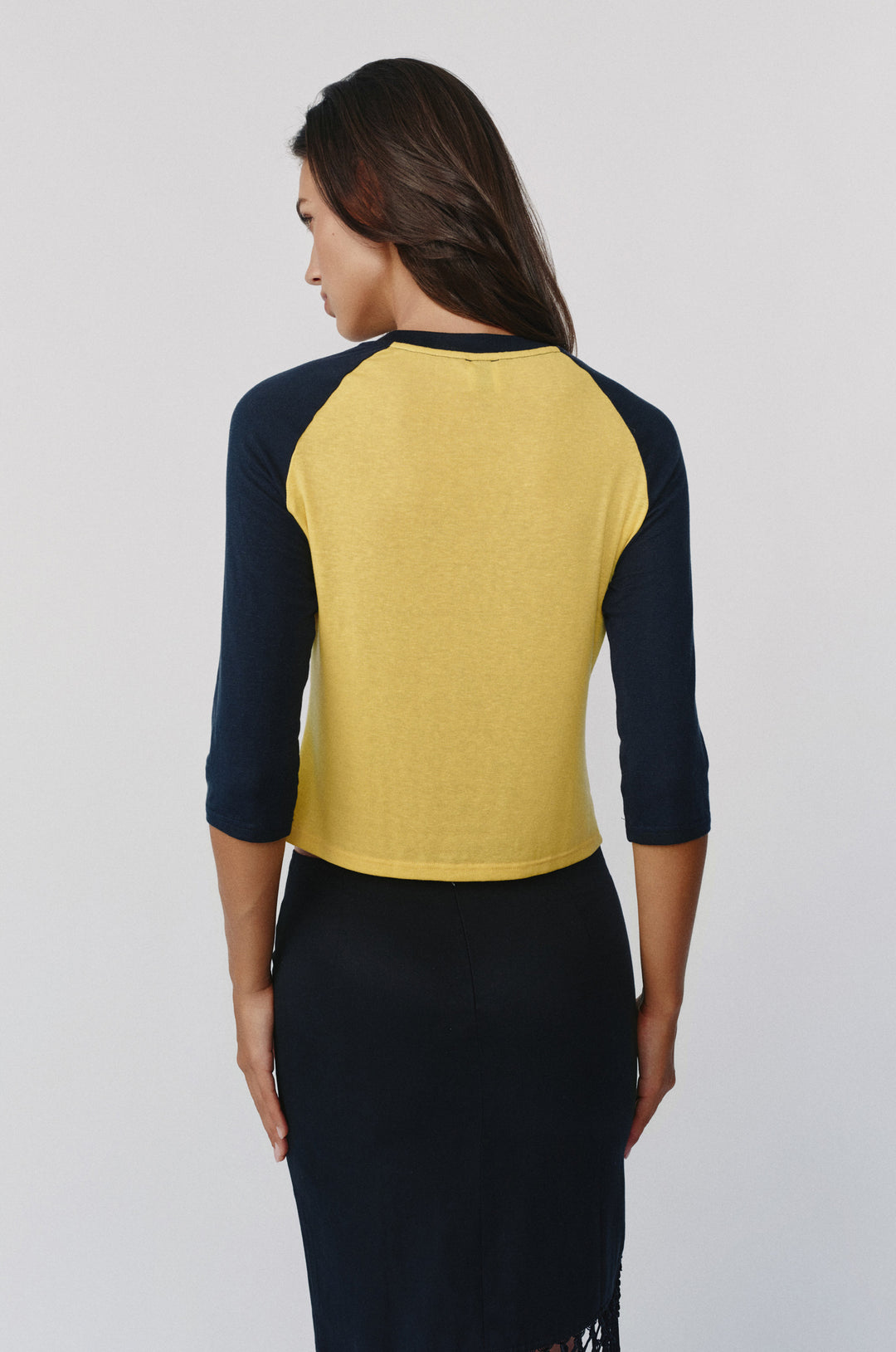 Back view of a Billie raglan tee with a yellow body, midnight navy sleeves, and a round neckline on a model.