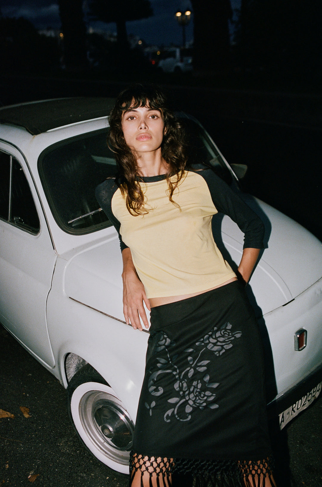 Model wearing a yellow and midnight navy Billie raglan tee with a round neckline, leaning against a white vintage car.
