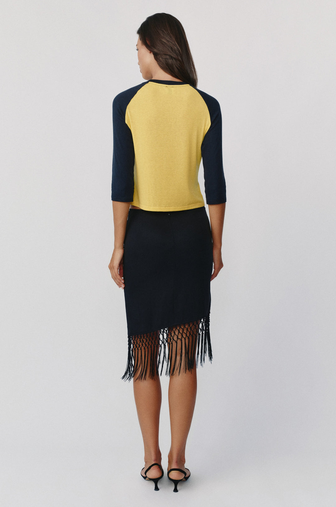 Woman wearing a yellow and midnight navy raglan tee with three-quarter sleeves and a black fringe-hem skirt.