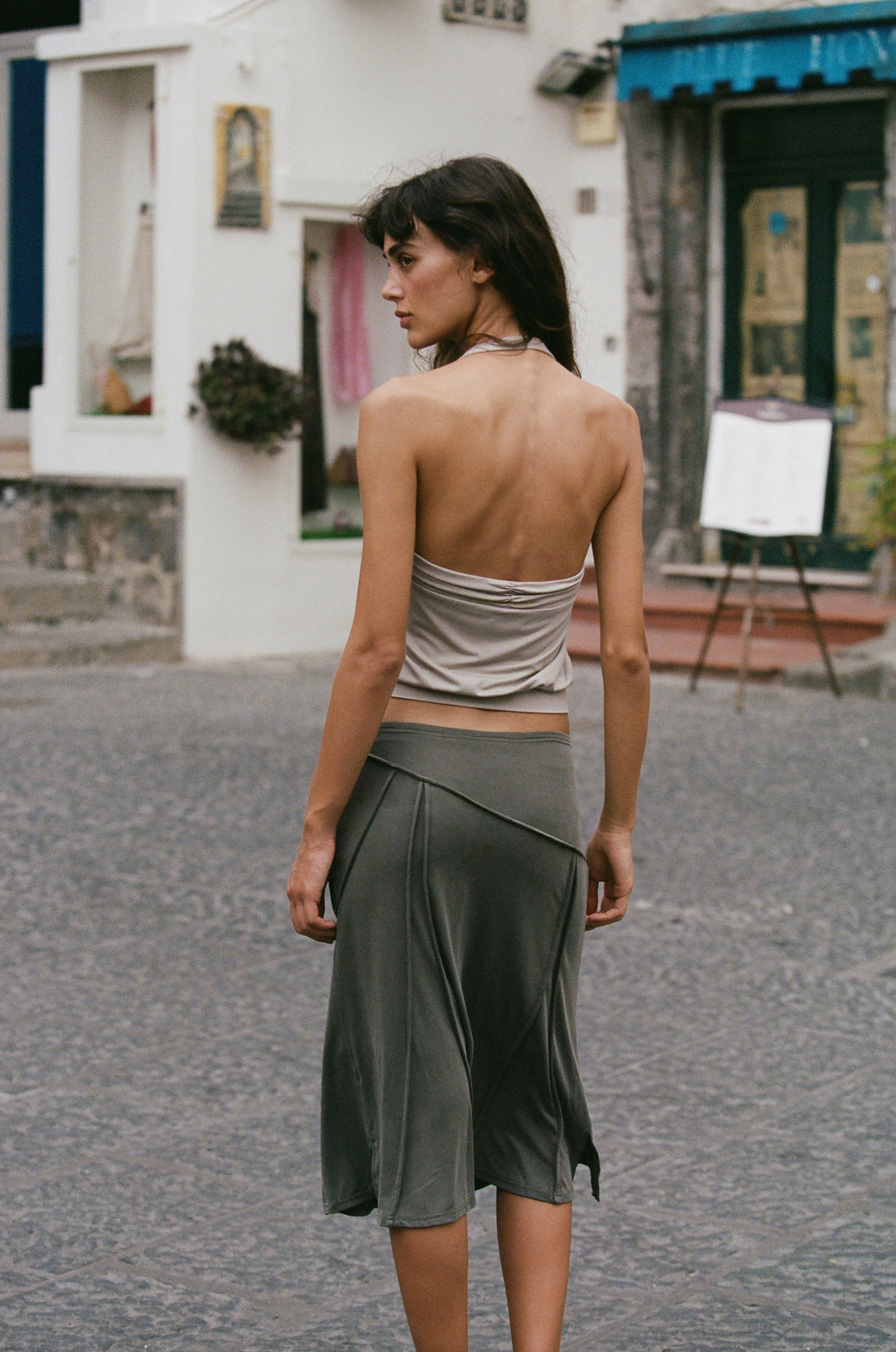 Stone-colored halter Briar Top with ruched detailing, worn with a dark olive midi skirt on a cobblestone street.