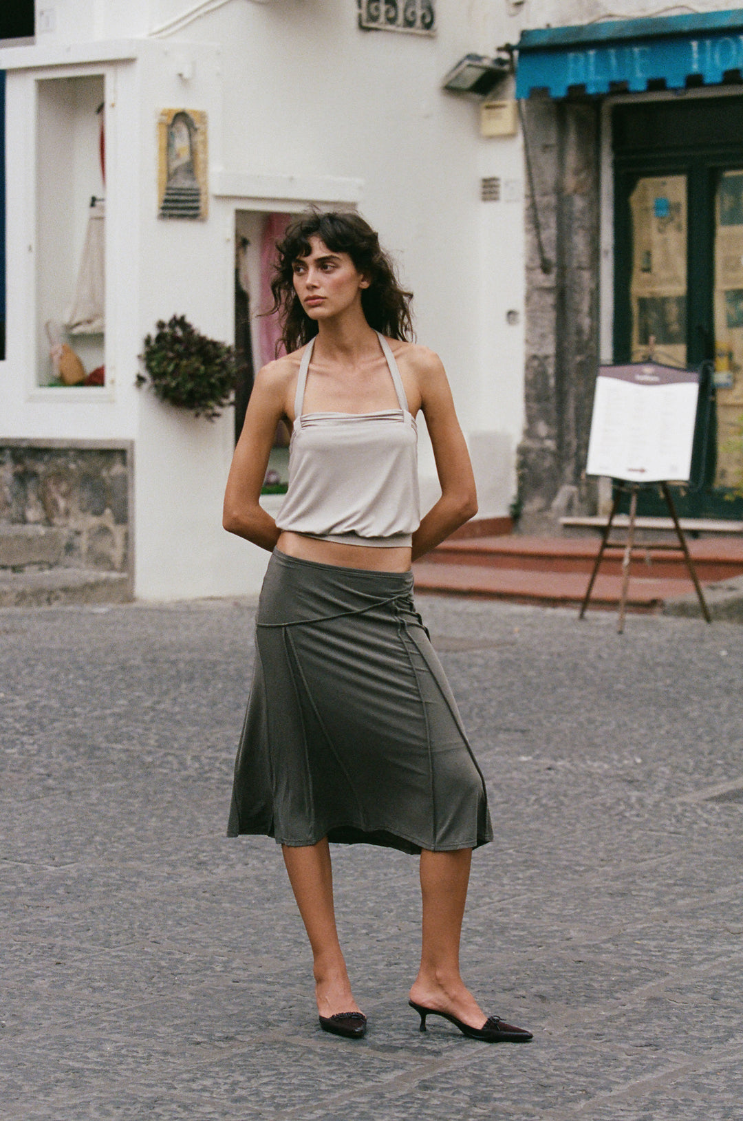 Stone-colored halter top with ruched detailing and a fitted hem, worn with a dark grey midi skirt.