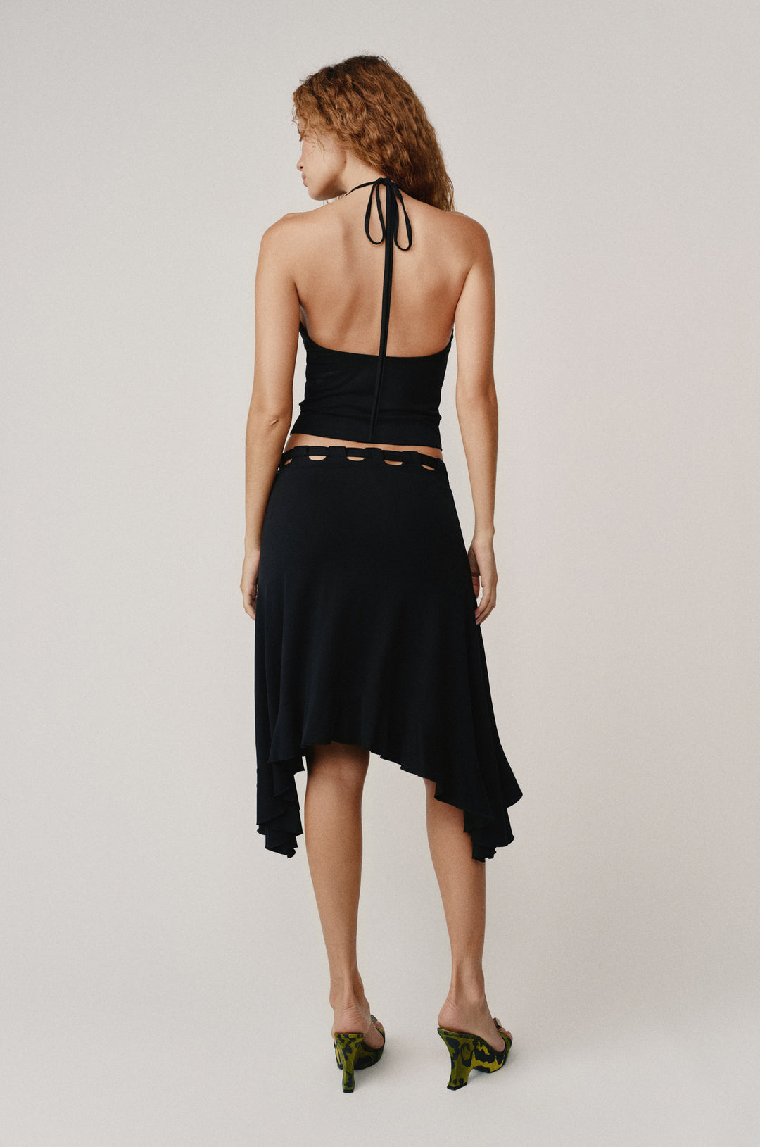 Black Carrie Top with self-tie halter neck, low back, and raw edge hem, worn by a woman from behind.