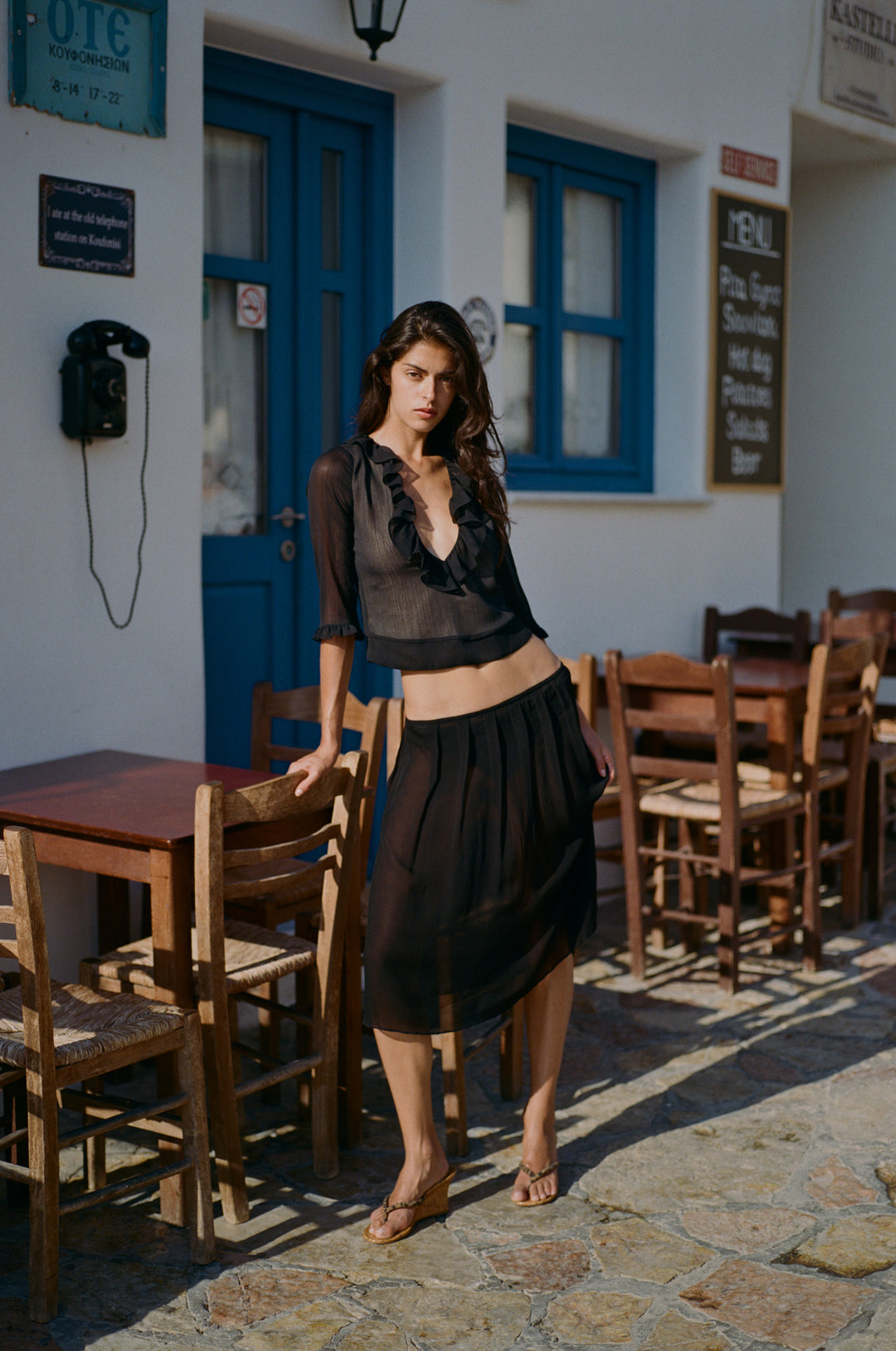 Model wearing a black low-rise midi skirt with a soft pleated silhouette and picot-edge elasticated waistband.
