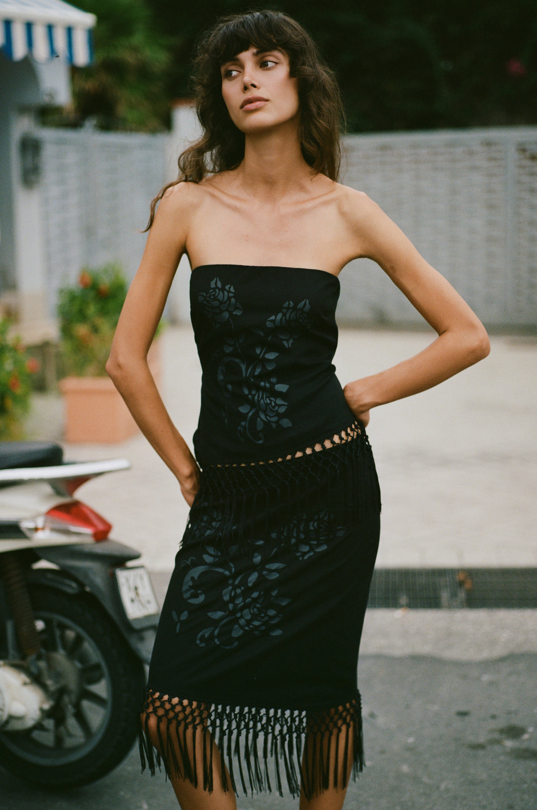 Model wearing a black low-rise Daria skirt with a custom floral print and a decorative macrame fringe hemline.