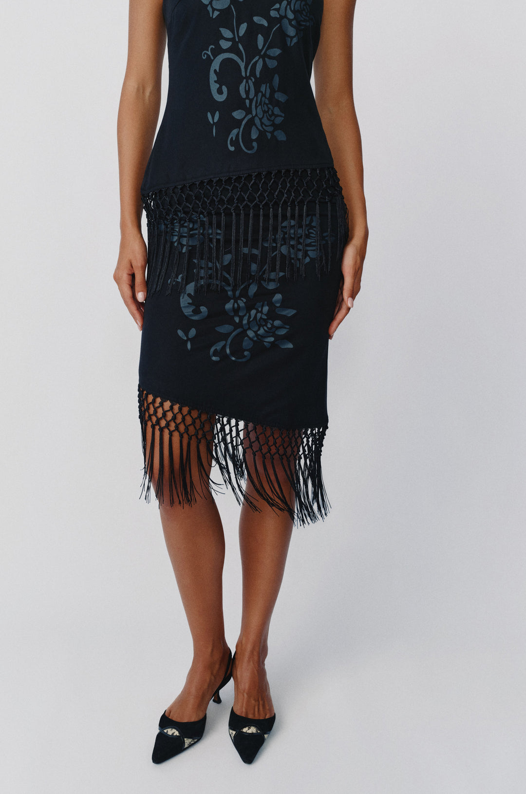 Black low-rise Daria skirt featuring a tonal floral print, asymmetrical hem, and decorative macrame fringe detailing.