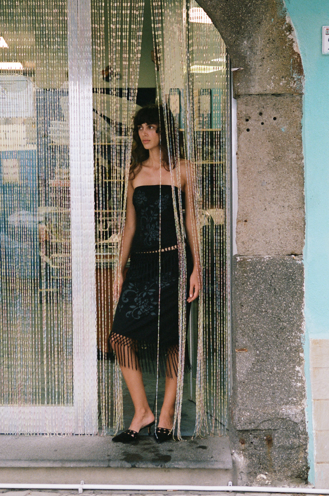 Black low-rise Daria skirt featuring a tonal floral print, asymmetrical hem, and macrame fringe detail.