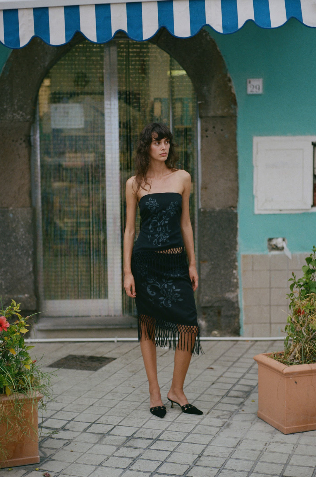 Black strapless Daria top featuring a dark floral print and an asymmetrical hemline with decorative macrame fringe.