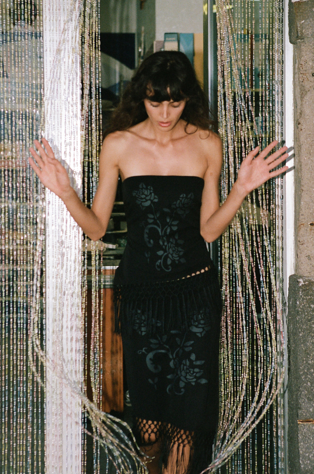 Black strapless Daria top featuring a dark floral print and an asymmetrical hemline with decorative macrame fringe.