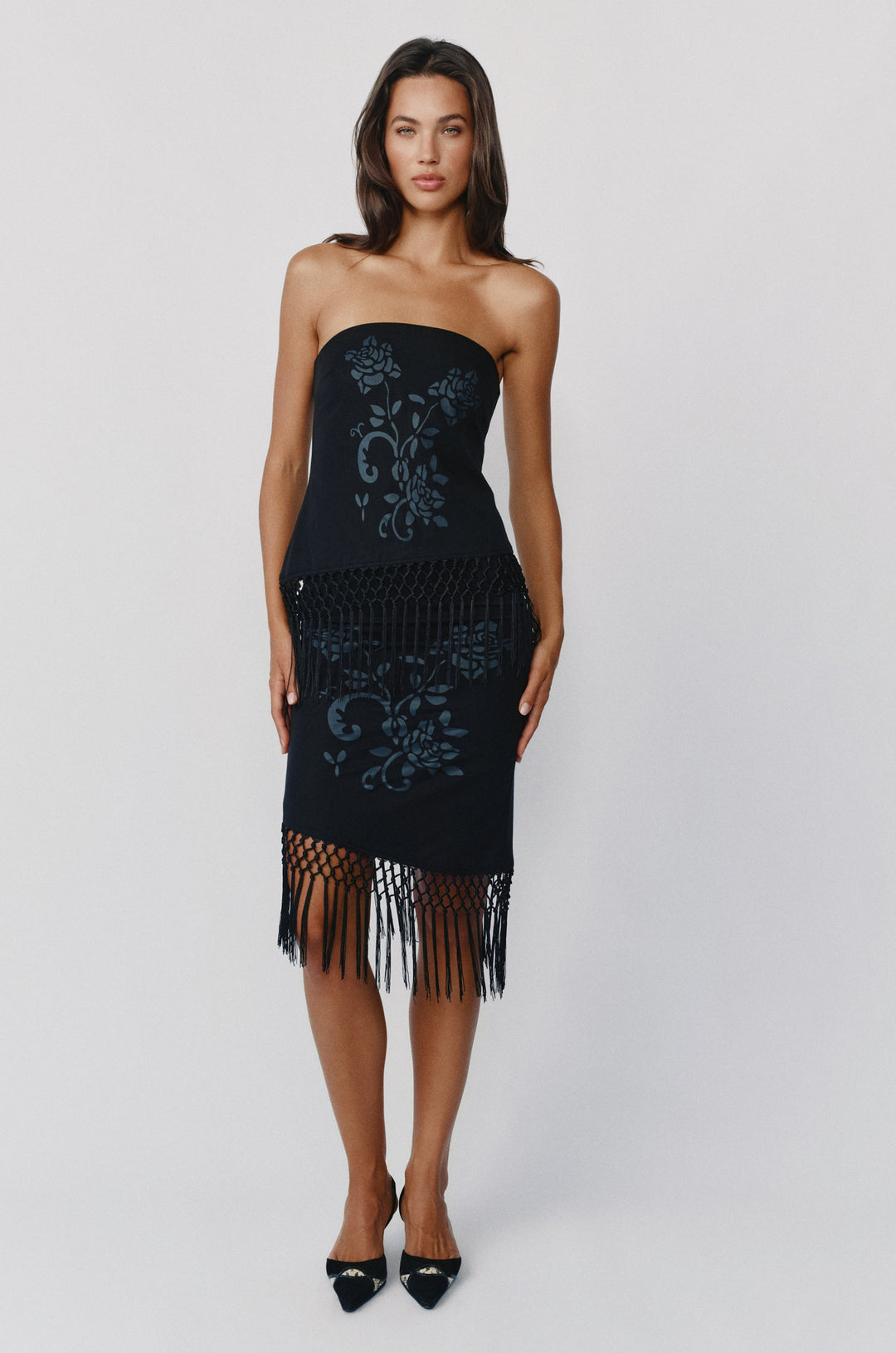 Black strapless Daria top with a floral print, asymmetrical hem, and decorative macrame fringe detailing.