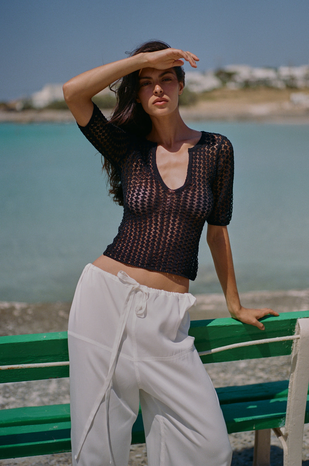 Black knitted Delilah top with a notched scoop neckline and half sleeves, worn with white trousers by the sea.