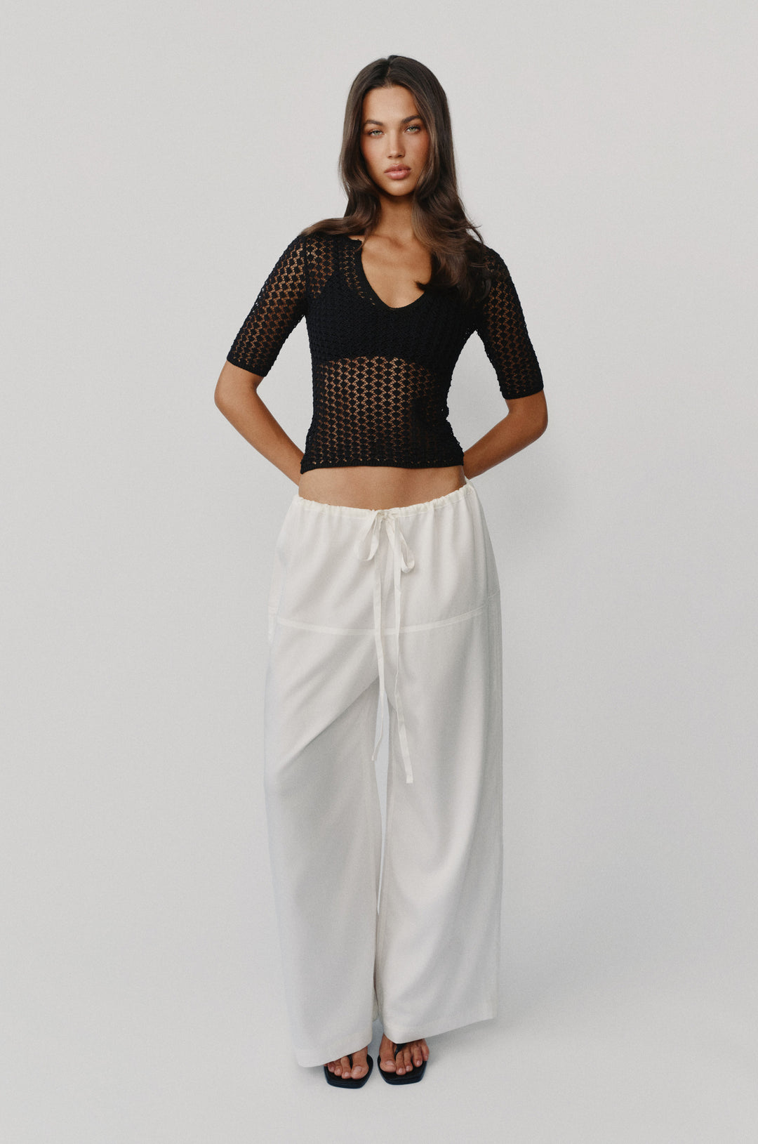 Black knitted Delilah top with notched scoop neckline and half sleeves paired with white wide-leg trousers.