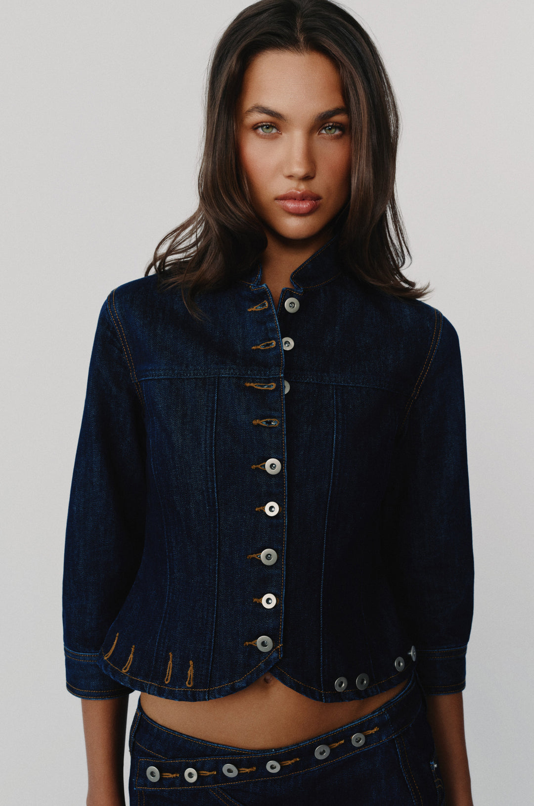 Indigo blue denim jacket with a stand collar, button-front closure, and 3/4 length sleeves on a model.