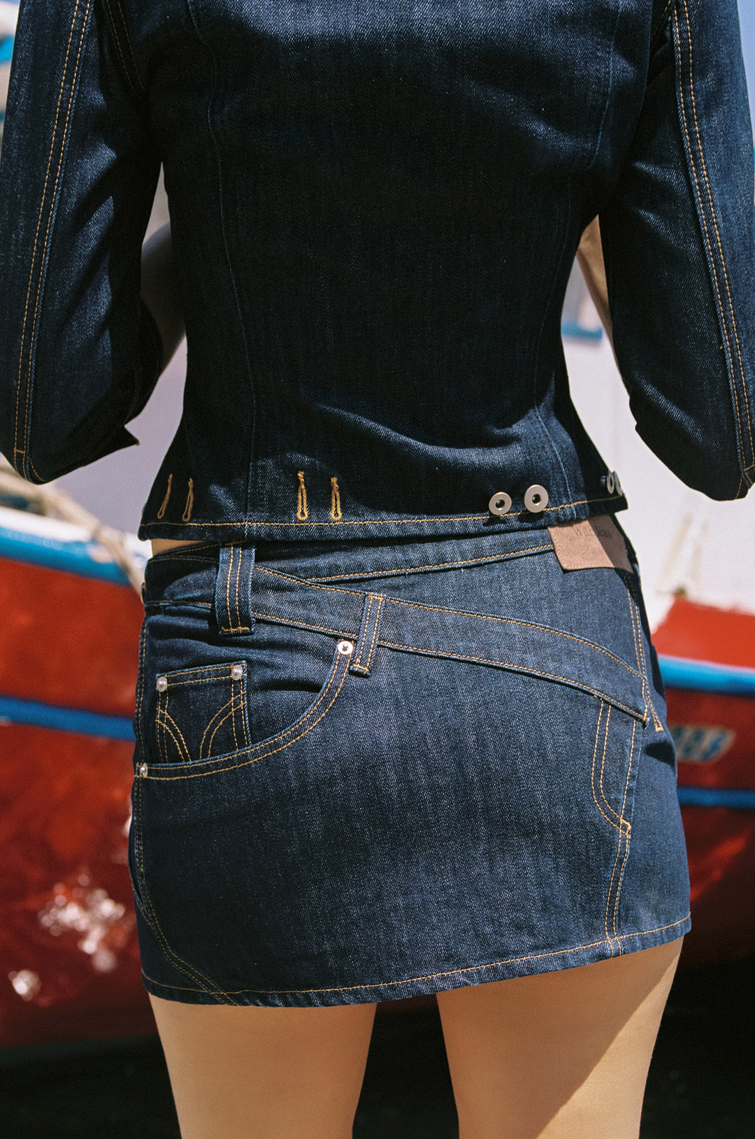 Indigo blue denim mini skirt with low-rise fit, asymmetric paneling, and contrast stitching details.