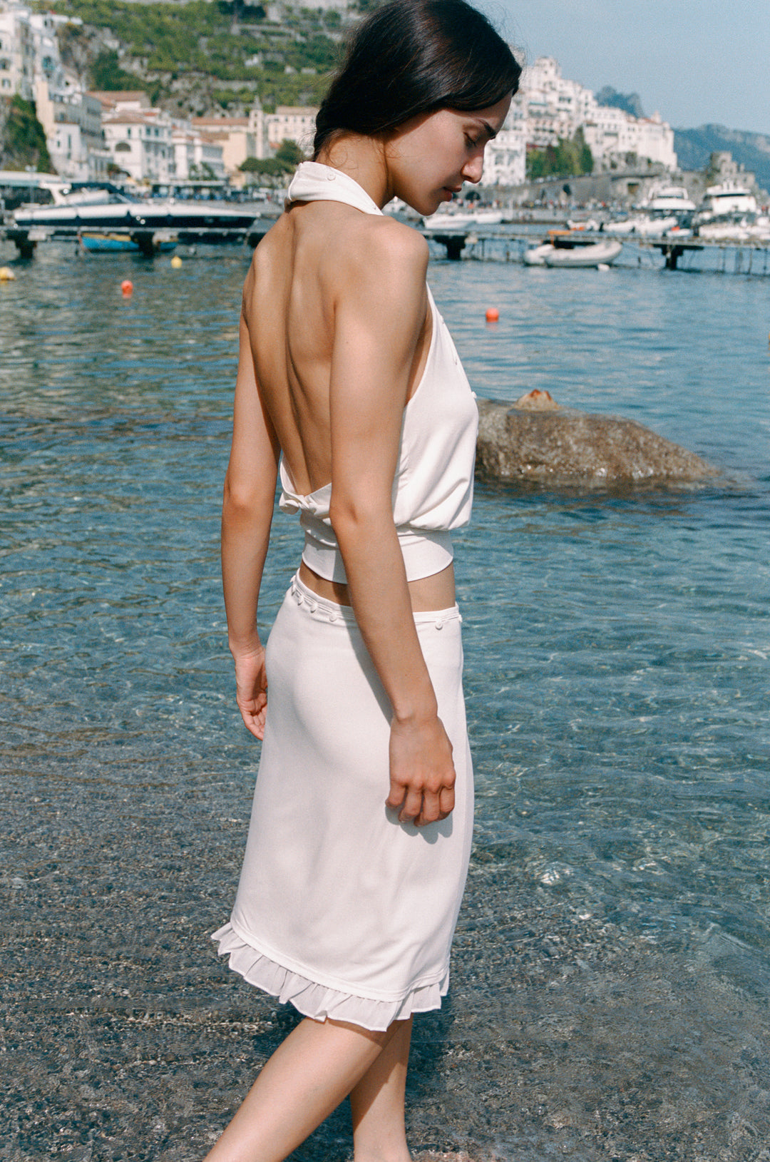 Ella Skirt: Off-white low-rise midi skirt with button detailing and frill trim, worn by a woman in water.