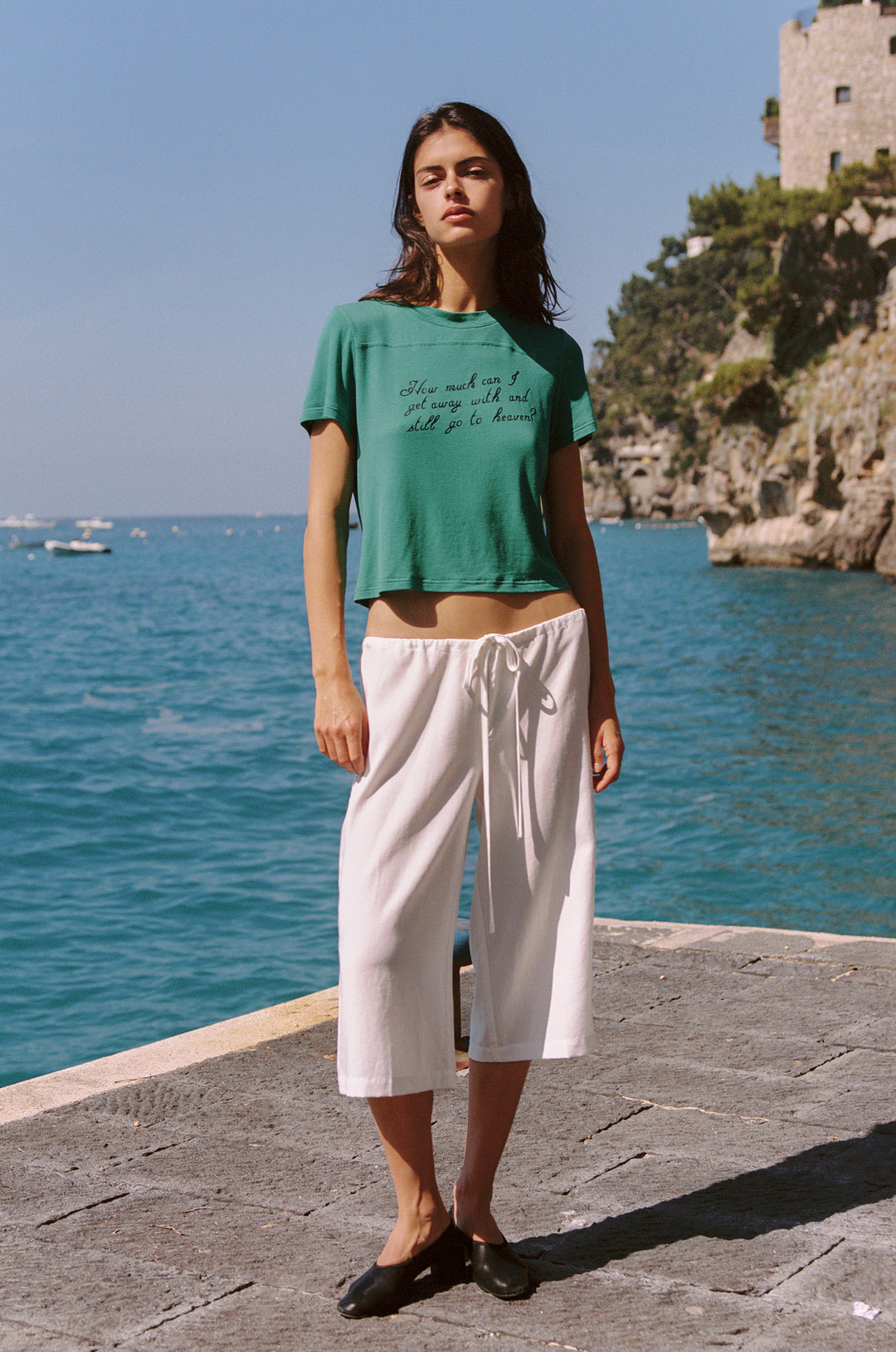 Woman wearing an emerald green Ellie Tee with a relaxed fit, short sleeves, and a round neckline, paired with white capris.
