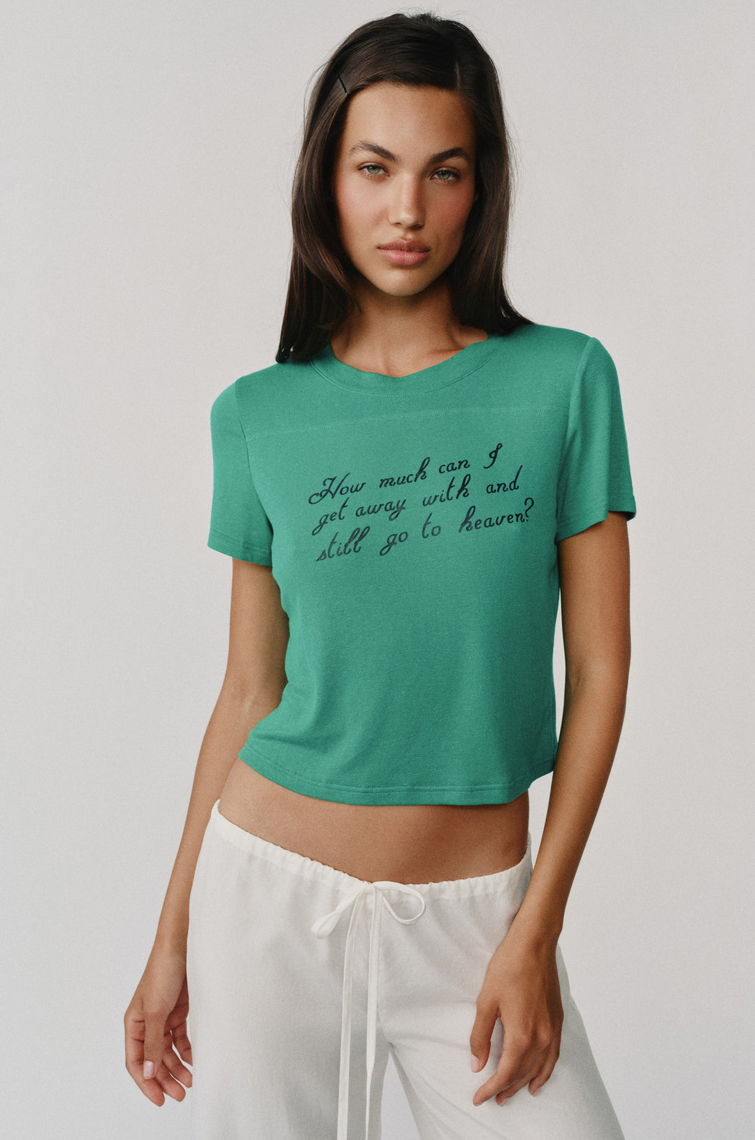 Woman wearing an emerald green Ellie Tee with "How much can I get away with and still go to heaven?" text.