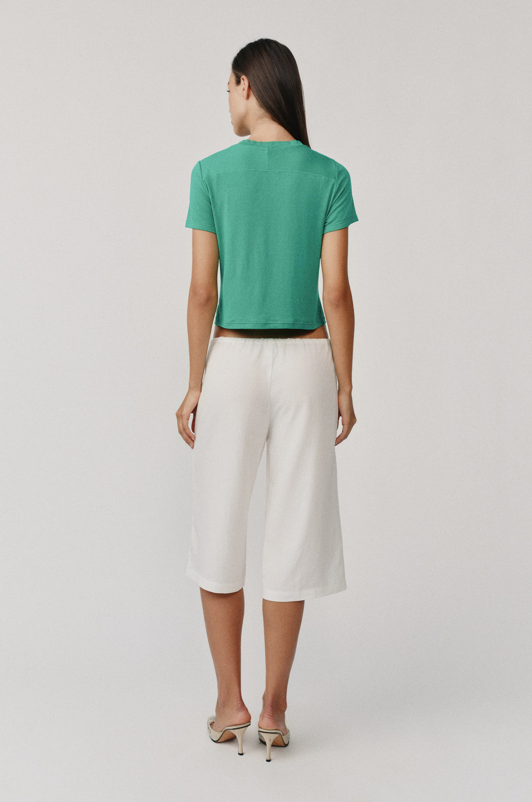Woman from behind wearing an emerald green Ellie Tee with short sleeves and a round neckline, paired with white shorts.