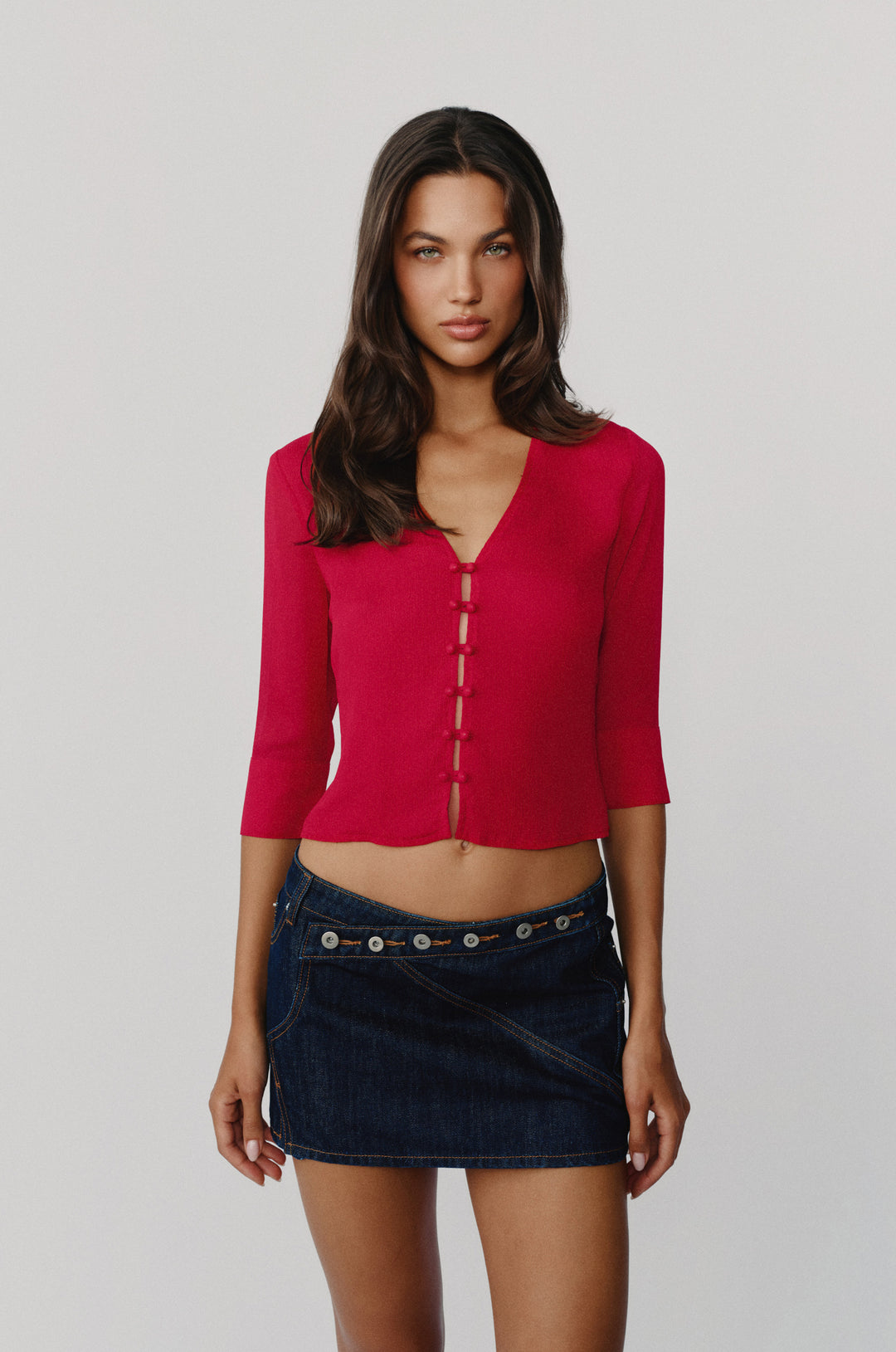 Red V-neck blouse with loop button-front closure and 3/4 length sleeves worn with a dark denim mini skirt.
