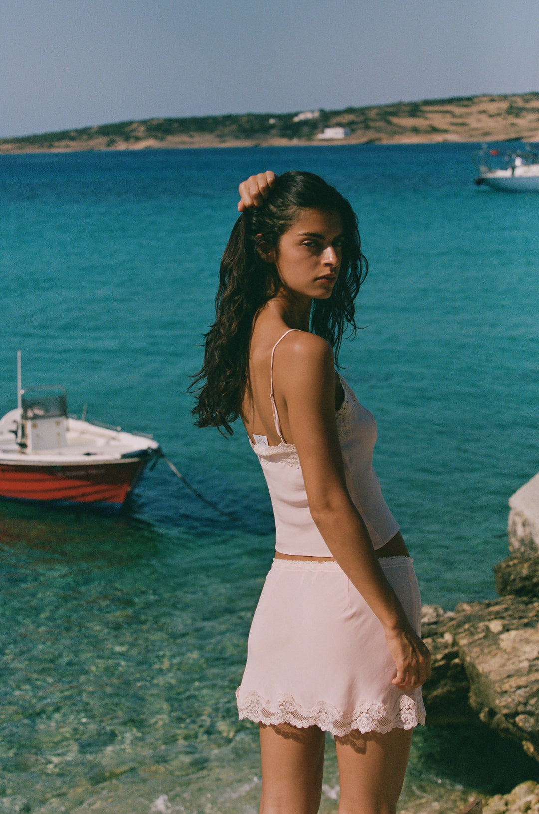 Pink Emerson mini skirt with a lace-trim elasticated waistband and hem, worn by a woman by the sea.