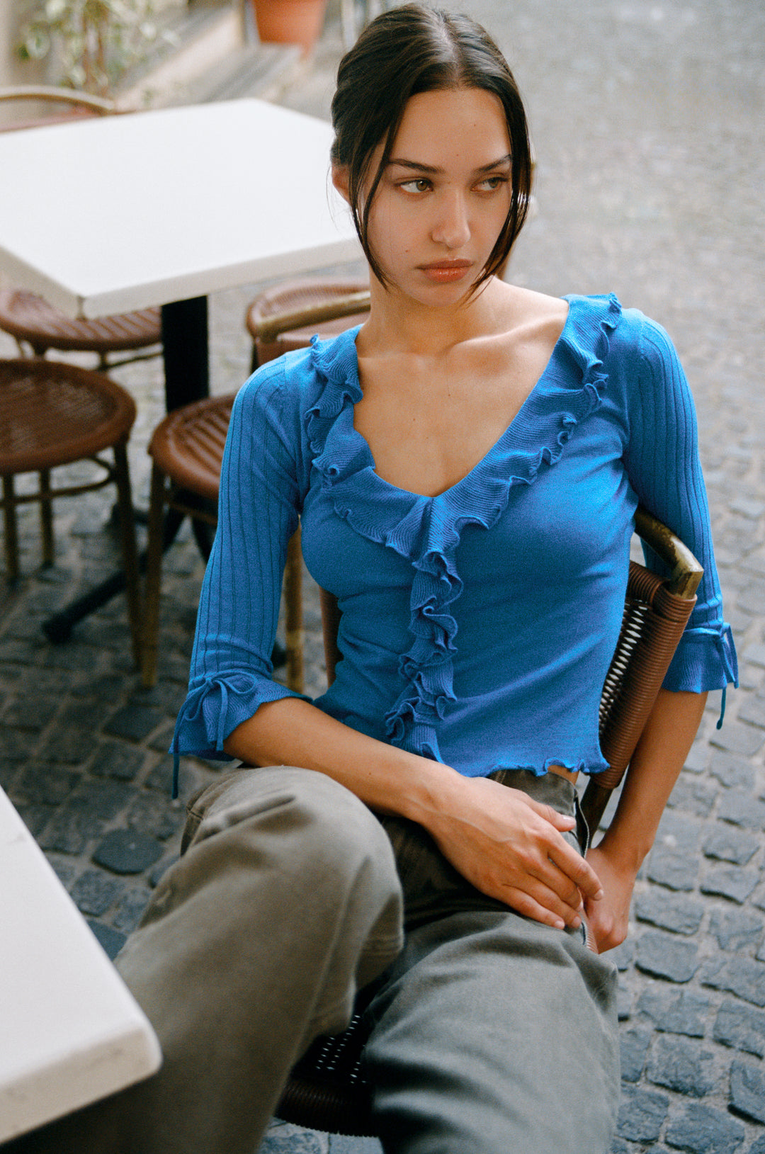 Model wearing blue knitted Emily Top with ruffle-trim neckline, 3/4 sleeves, and tie-detail cuffs.