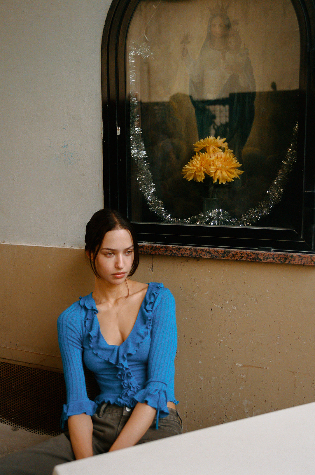 Woman in blue knitted Emily Top with ruffle-trim neckline, 3/4 sleeves, and ruffle cuffs with ties.