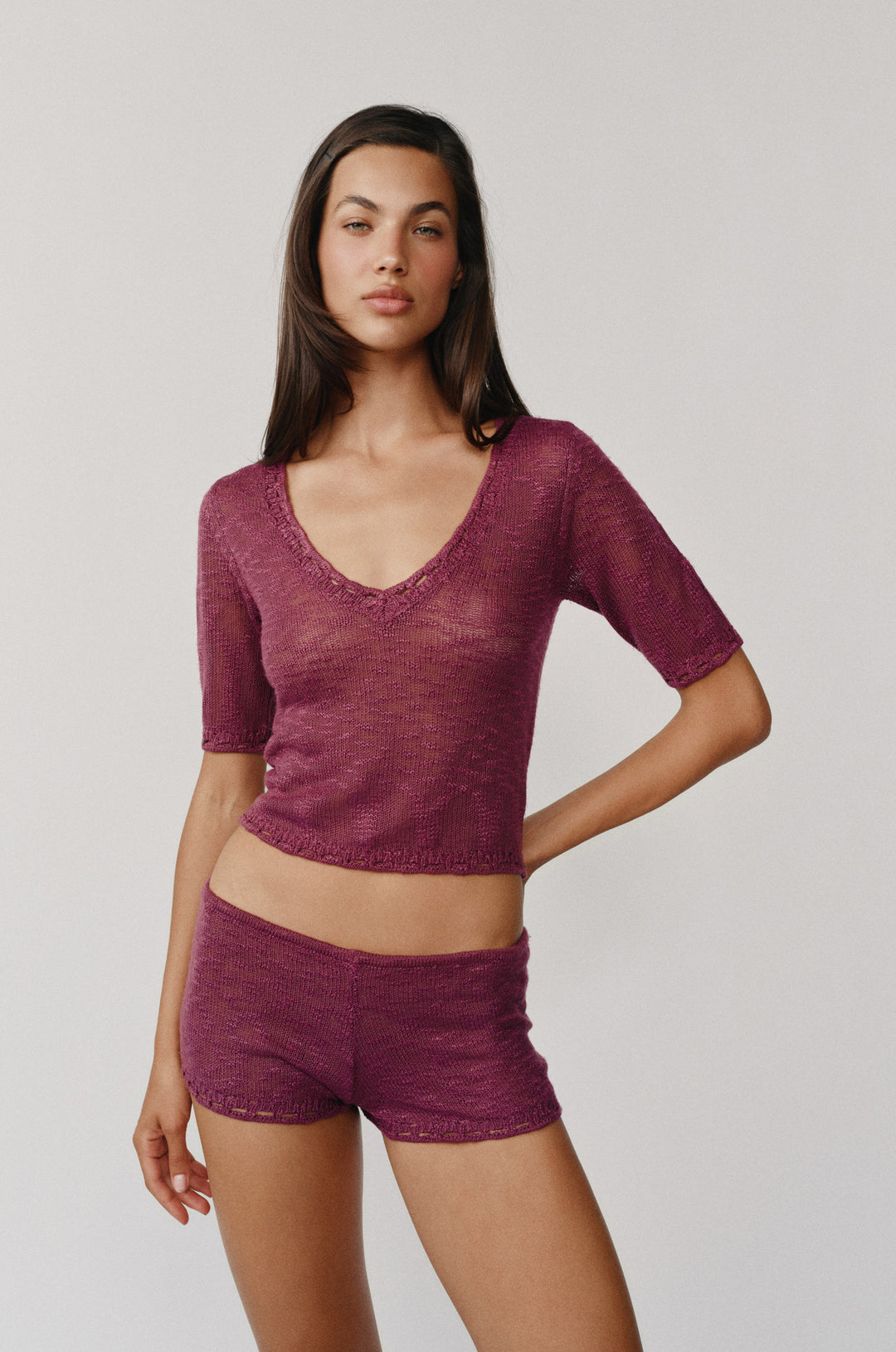 Model wearing Flora Shorts in Plum, low-rise knitted shorts with elasticated waistband and crochet trim.